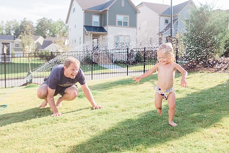 toddler and dad playing in the sprinkler photo
