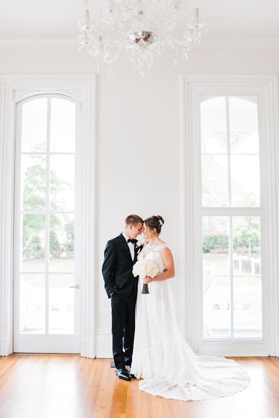 merrimon wynne bride and groom beside tall windows photo