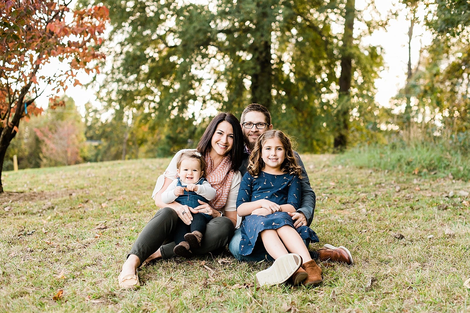 wake forest family of four sitting on a grass hill photo