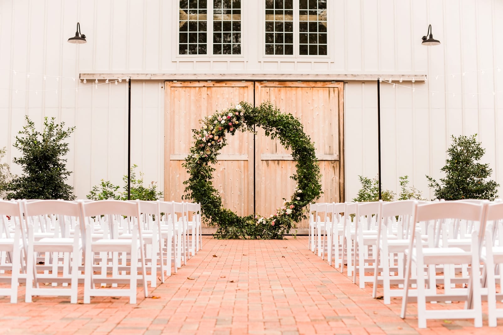Barn of Chapel Hill ceremony space with white chairs and large circle floral installation in front of wooden barn doors photo