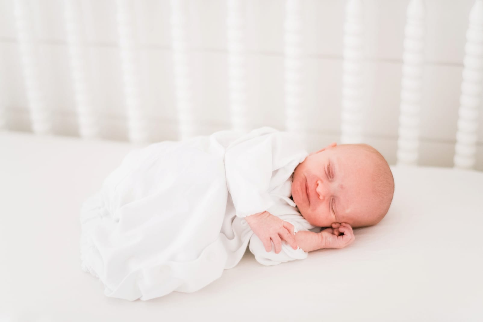 Apex newborn girl laying in her all white crib photo