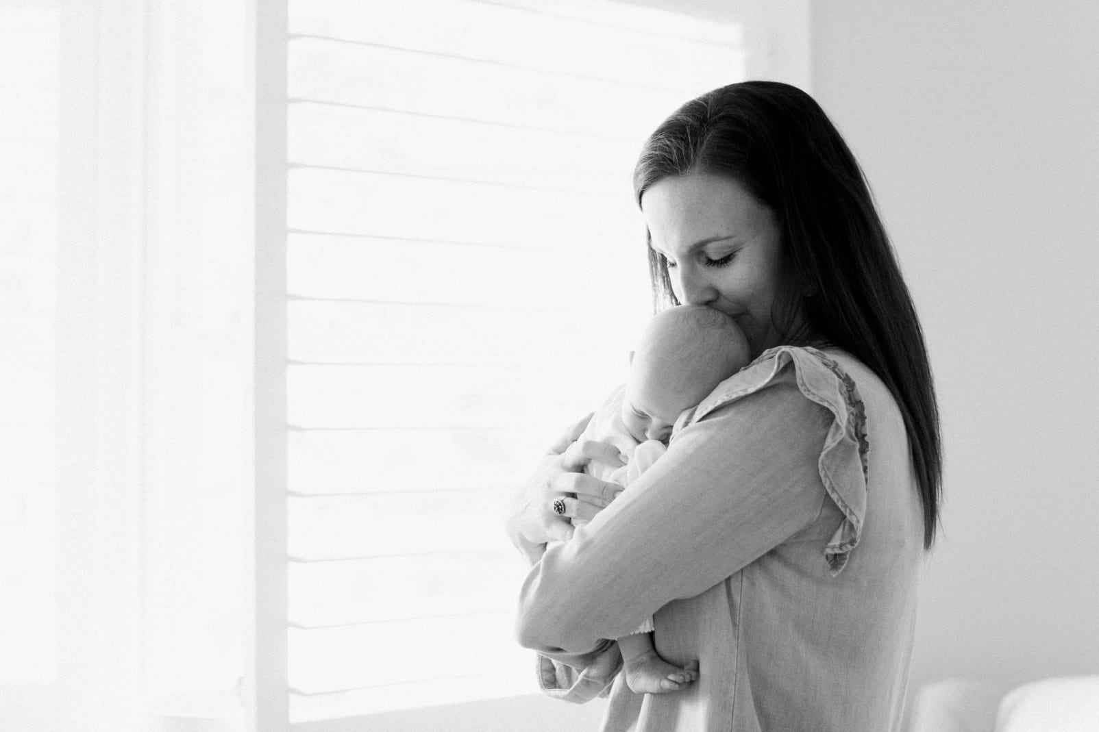 Apex mother kissing her newborn daughter on her head in front of the window photo