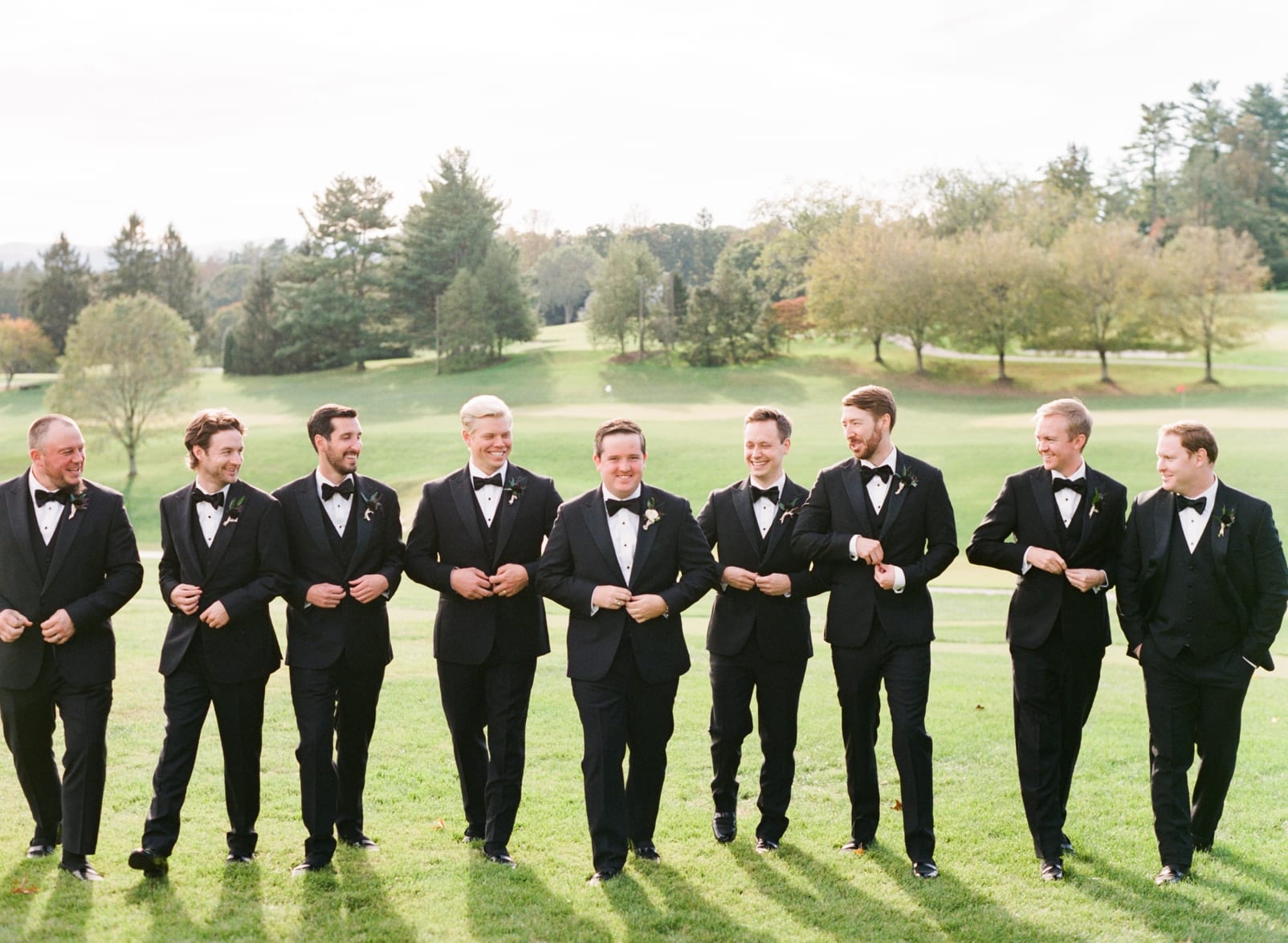 The Black tux groomsmen and groom in black tuxes walking while buttoning their jacket photo