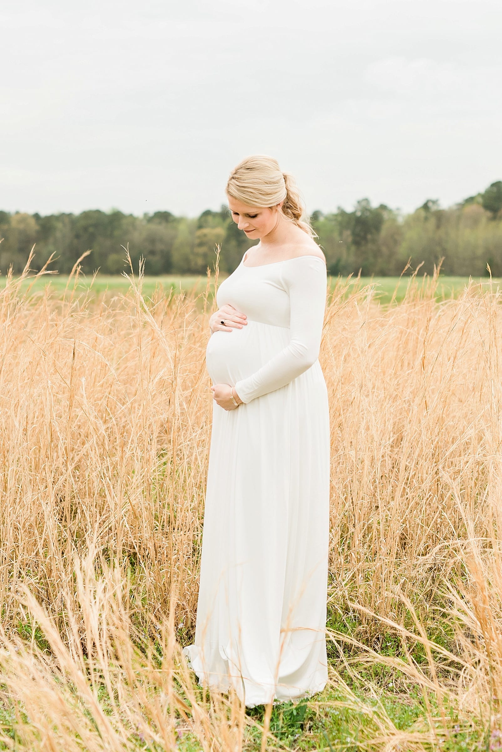 Wake Forest maternity session mother in long off-white dress standing in a wheat field photo