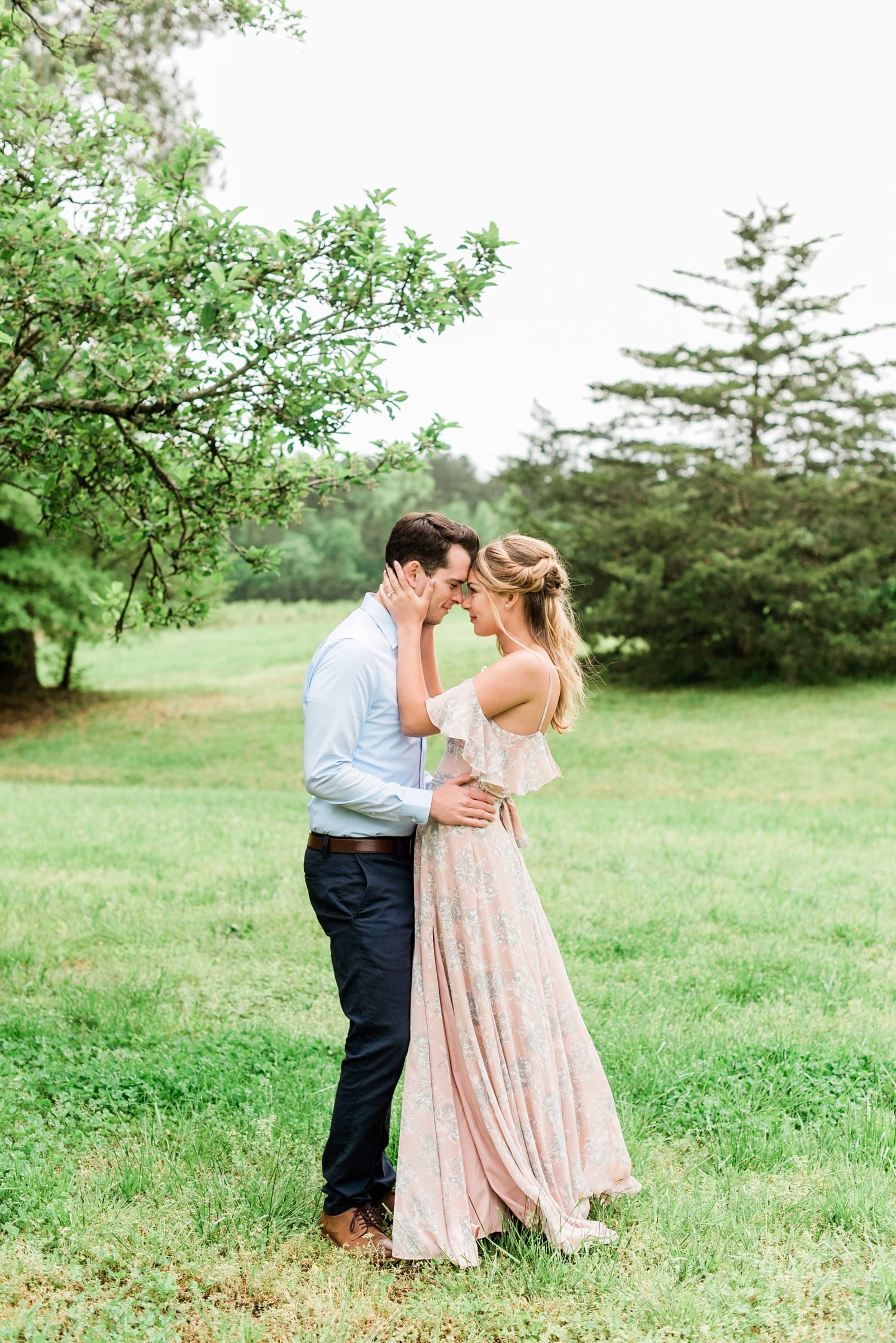 Spring engagement with bride in blush pink long dress and groom in light blue button down embracing together photo