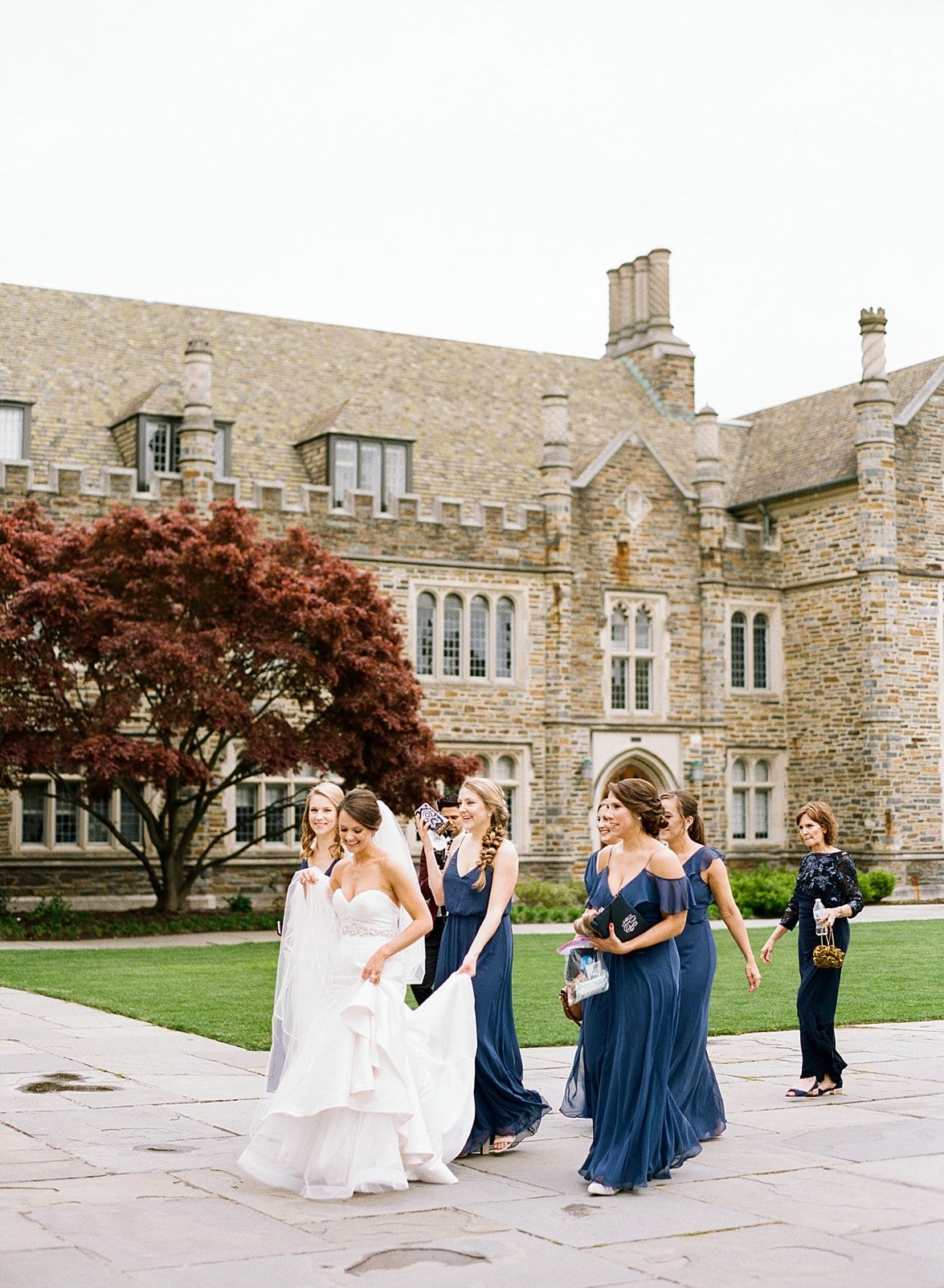 Duke Chapel bride walking to ceremony with her bridesmaids in long navy blue dresses helping her walk photo