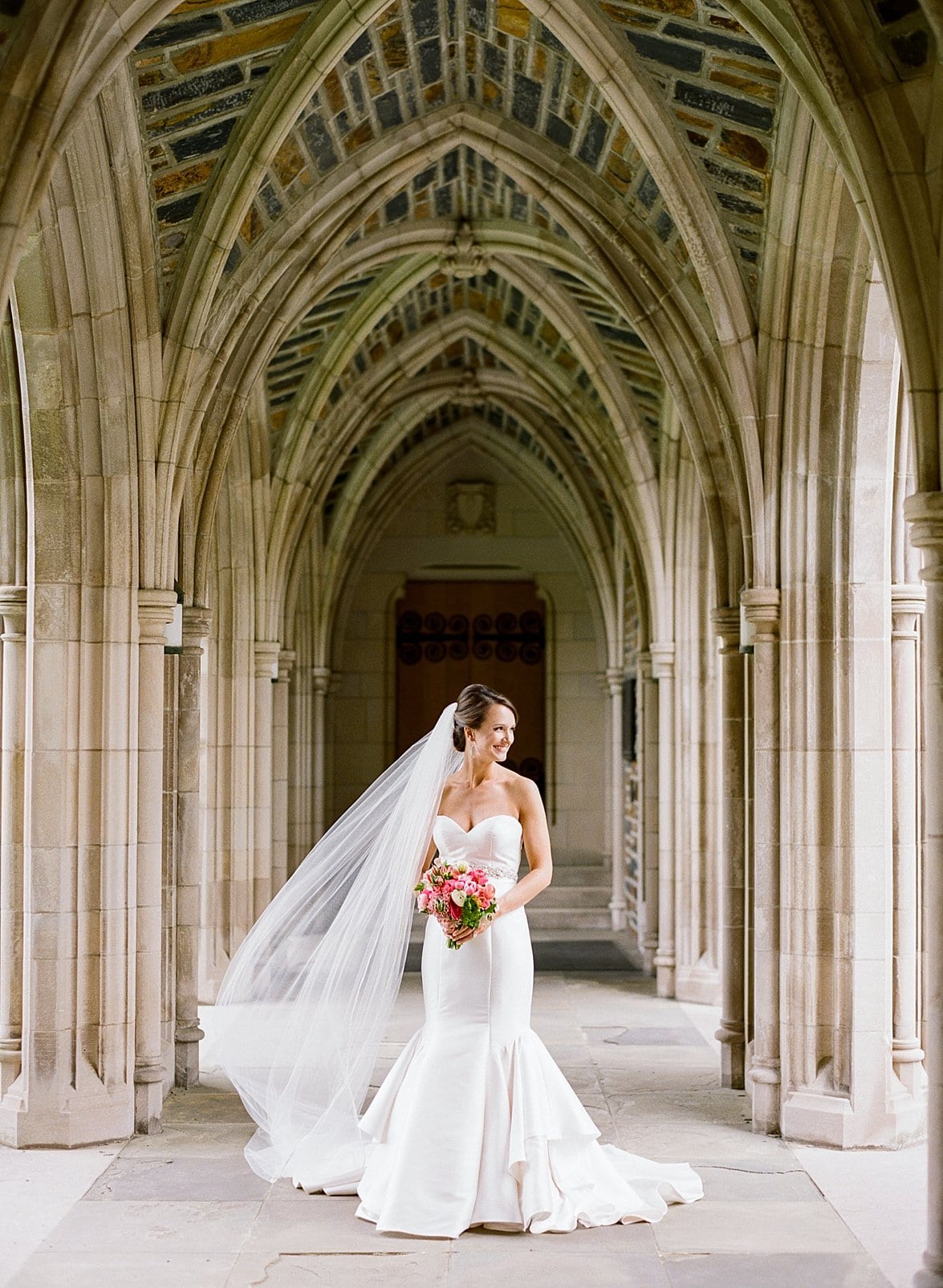 Duke Chapel bride standing under the Duke Chapel arches with her veil blowing to the side photo