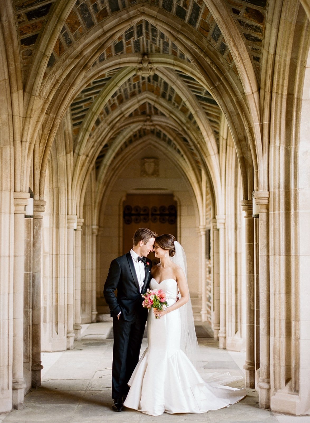 Duke Chapel bride and groom looking at each other standing under Duke Chapel stone arches photo