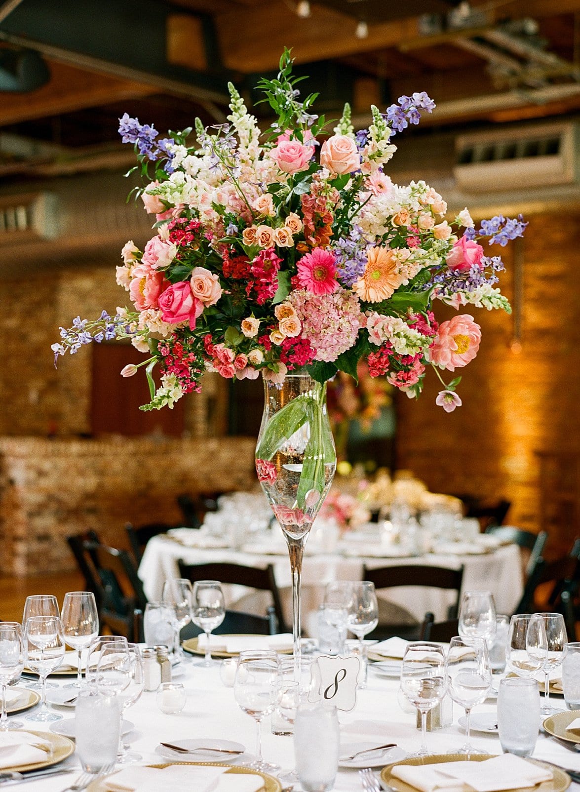 Artfully Arranged large round center piece with bright flowers in a tall clear glass vase photo