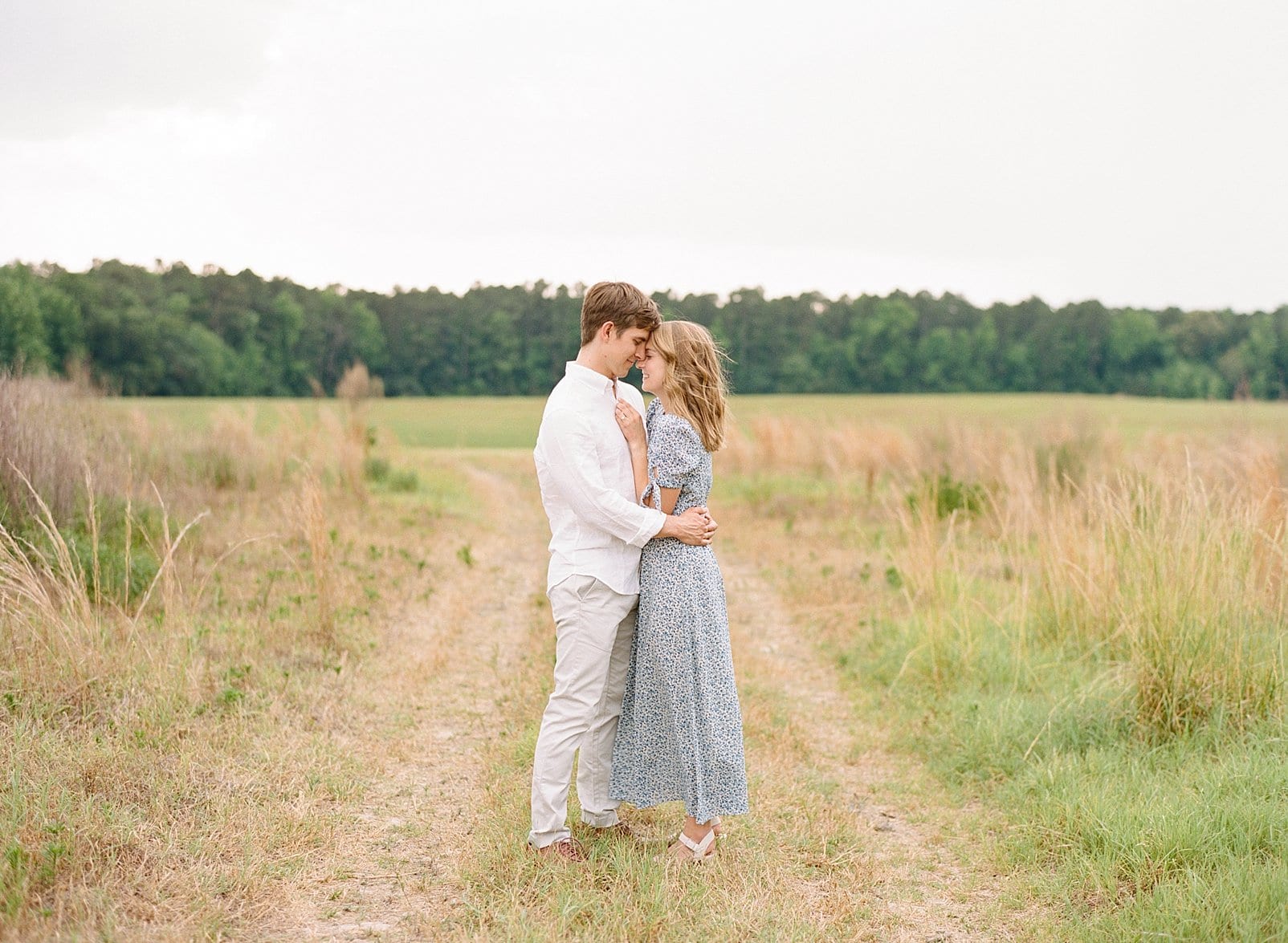 Raleigh Film engagement portraits couple standing together in the middle of a grass road photo