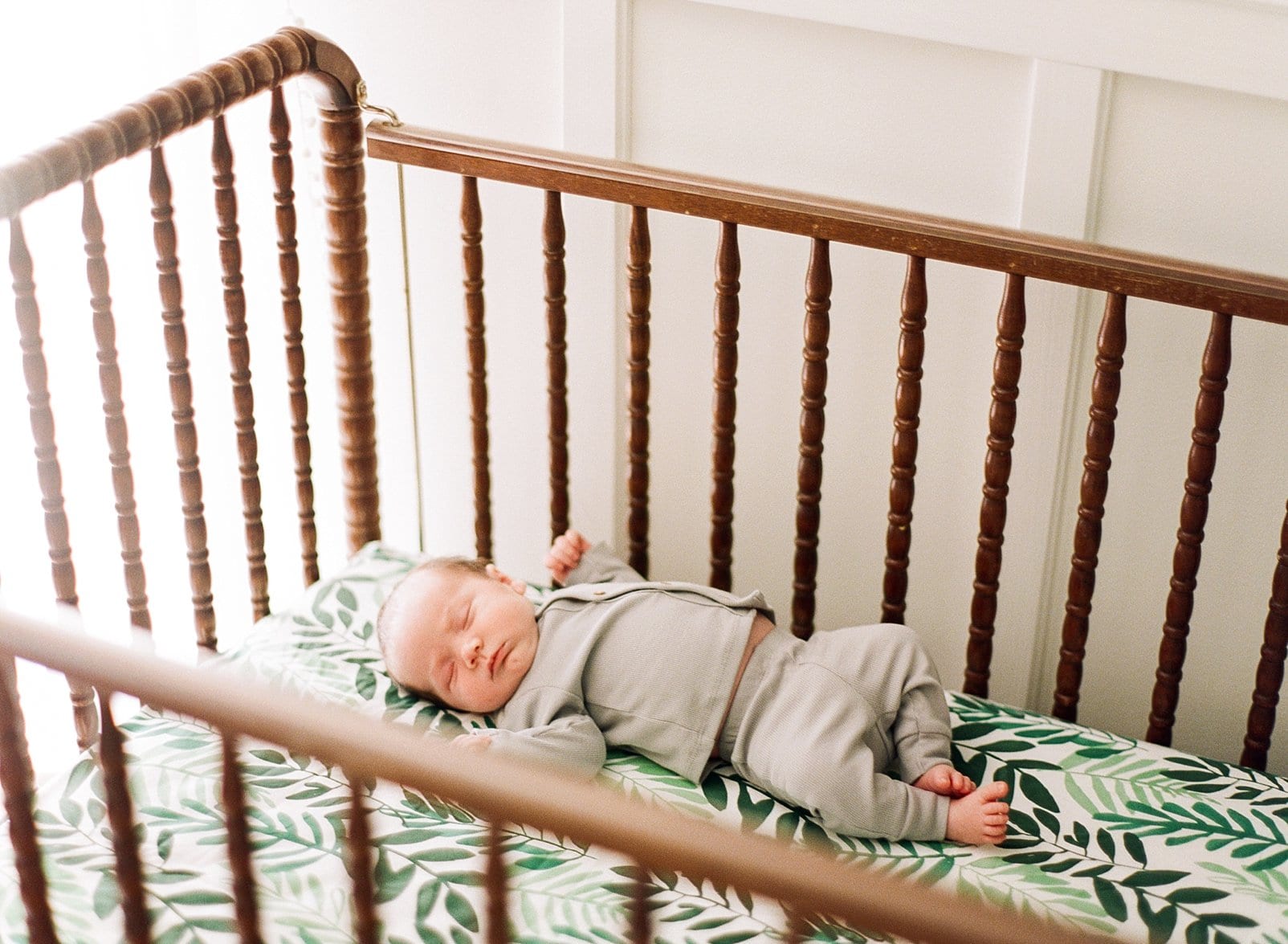 Raleigh newborn boy in a tan outfit laying in his brown wooden crib with greenery on his sheet photo