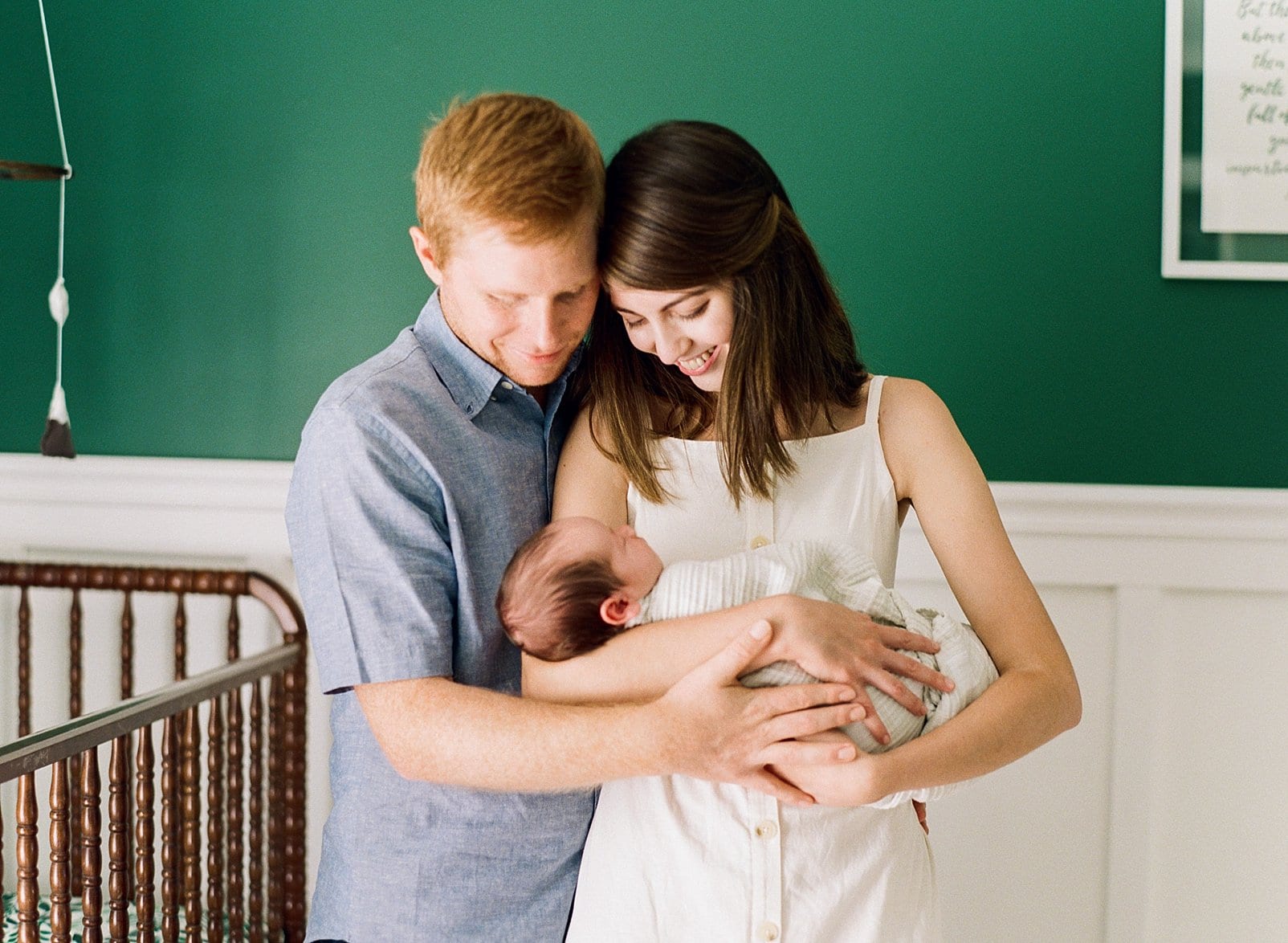 Raleigh mother and father holding their newborn son with his emerald green nursery wall behind them photo