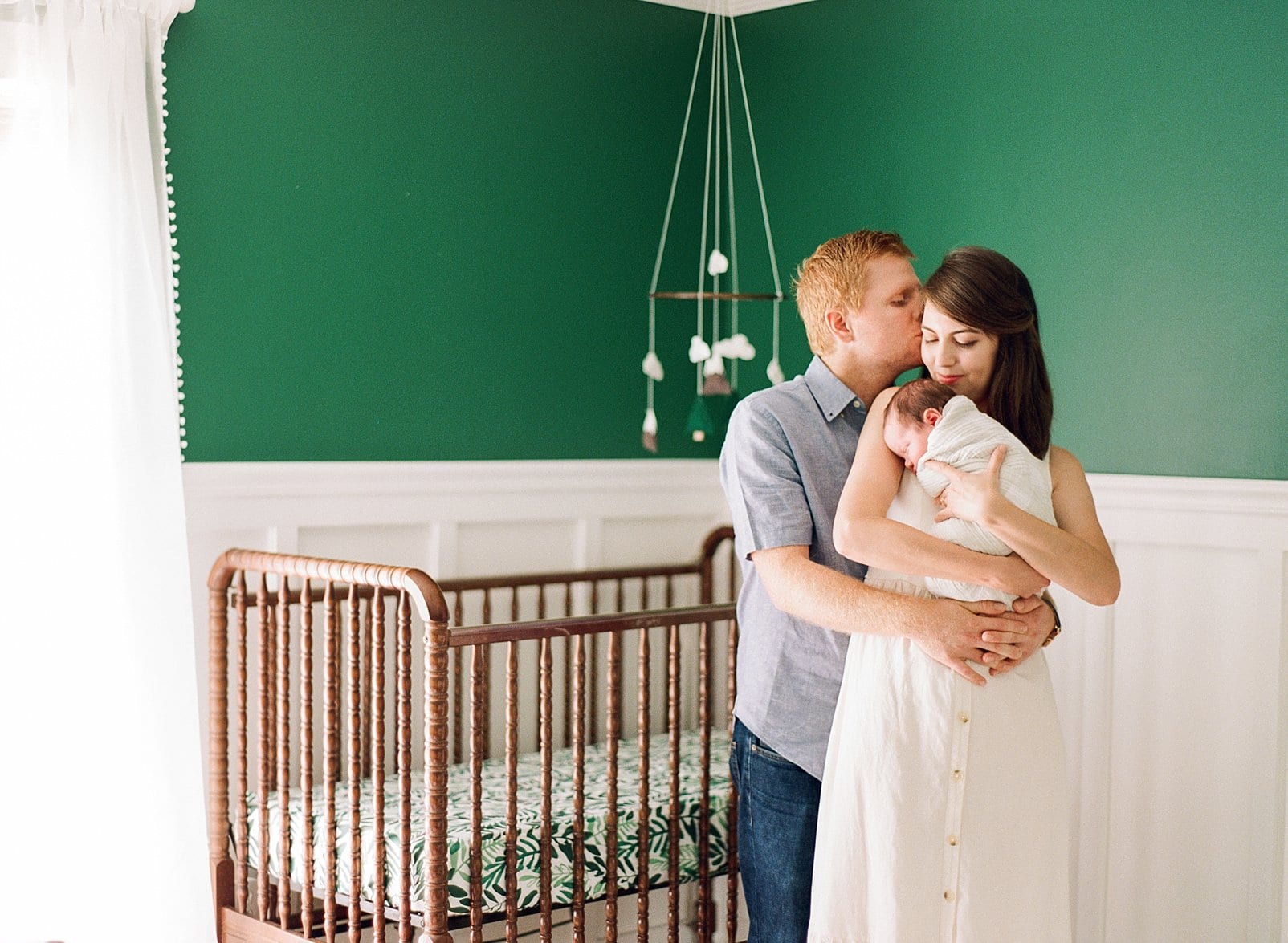 Raleigh mother and father holding their newborn son standing in front of his wooden crib photo