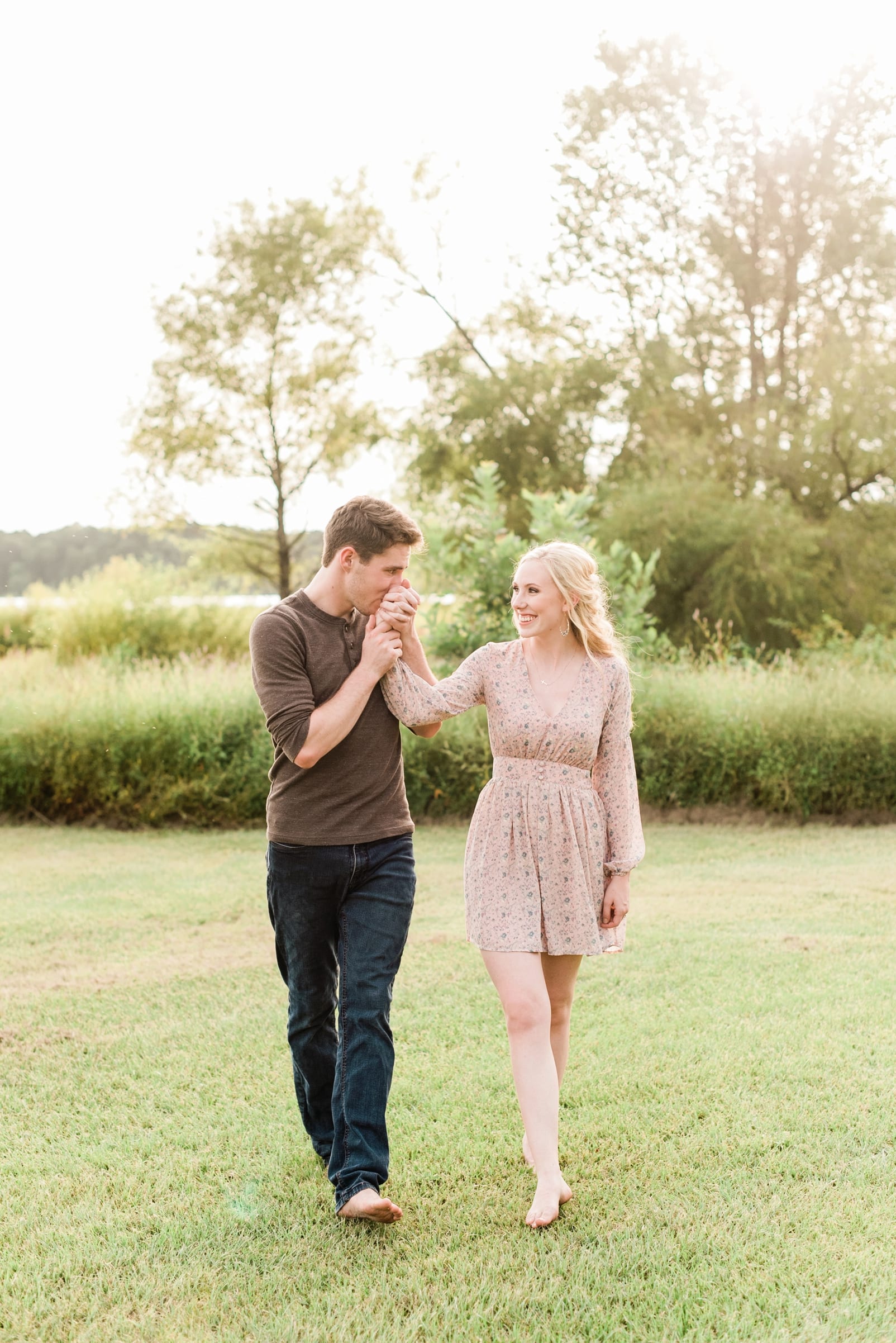 NC engagement pictures guy kissing his finance's hand while they are walking through a field photo