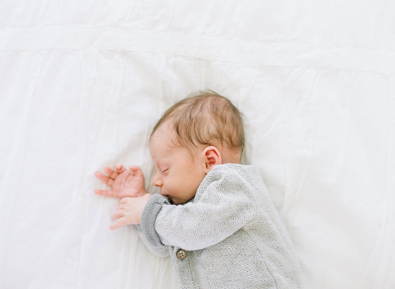 Raleigh newborn baby boy in a gray outfit laying on his side on a white bed photo