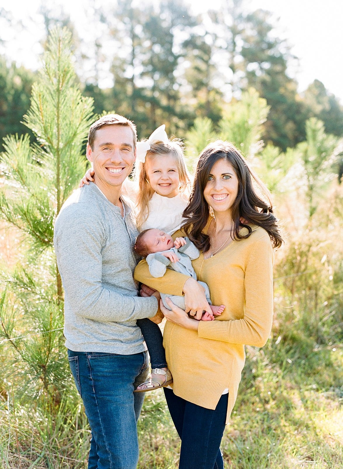 Raleigh family of four with their newborn son in front of young pine trees photo
