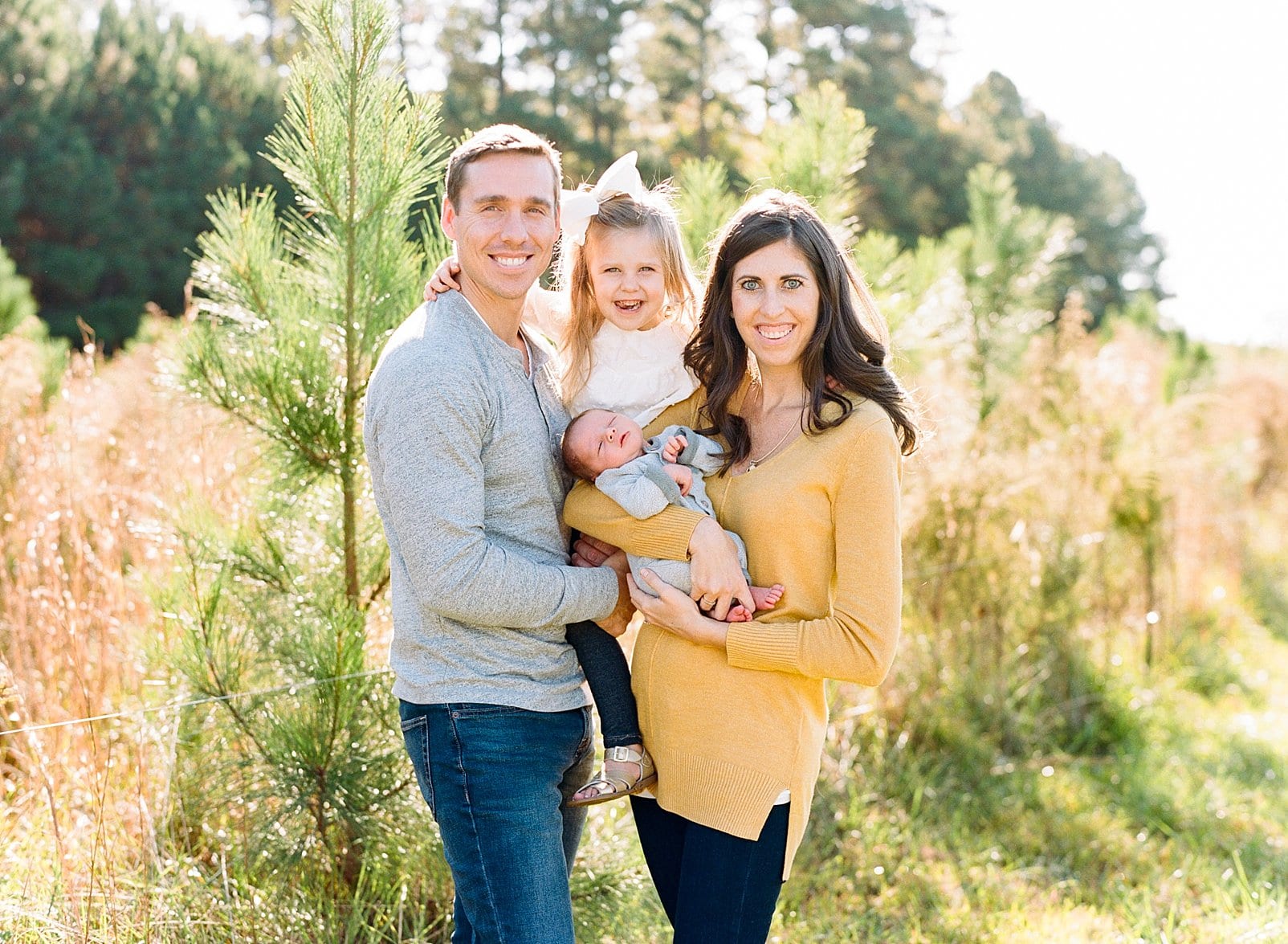 Raleigh outdoor film family session with newborn son and three year old daughter standing in front of a young pine tree field photo