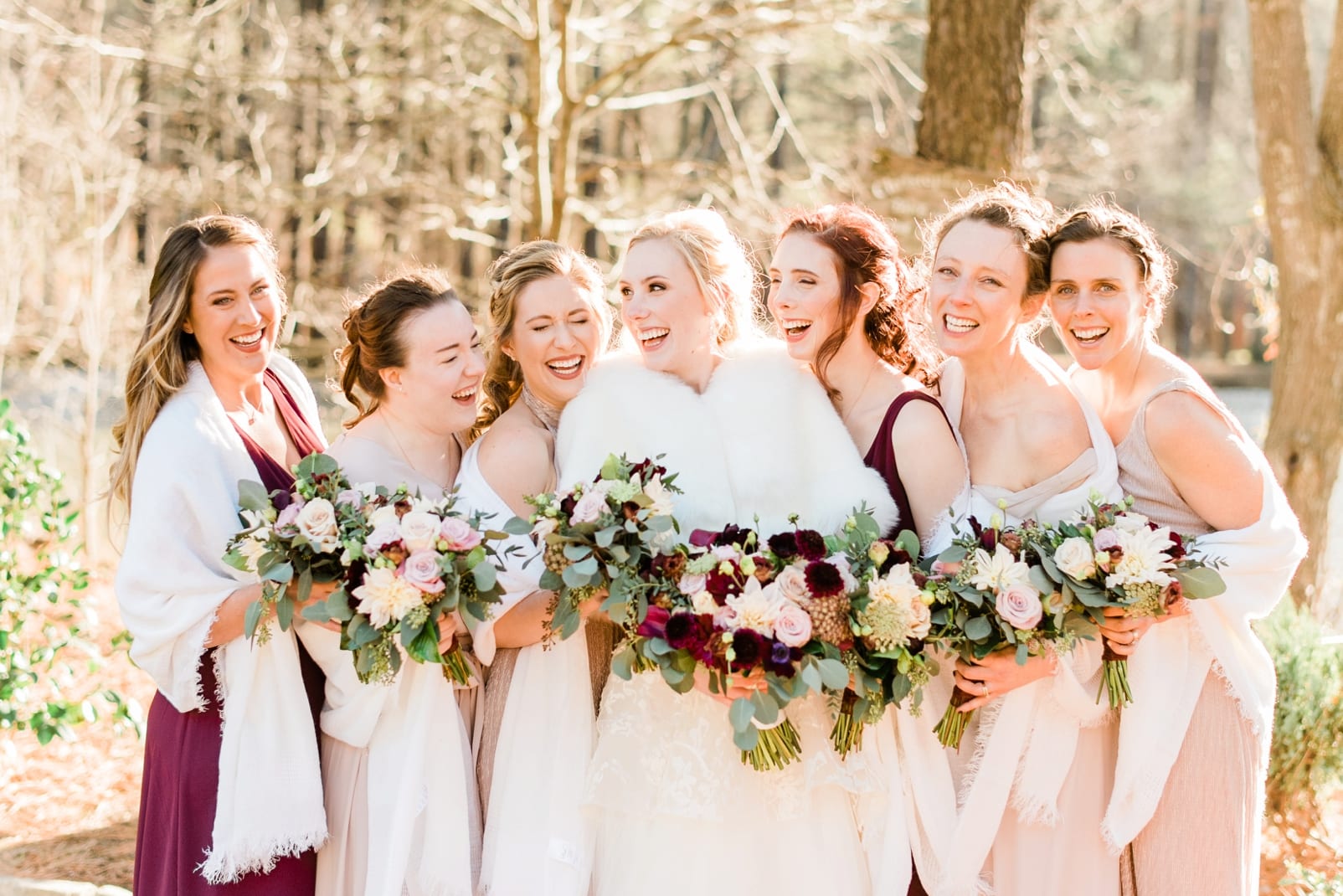 Angus Barn bride laughing with her bridesmaids in long pink pink and maroon dresses with cream shawls around their shoulders photo