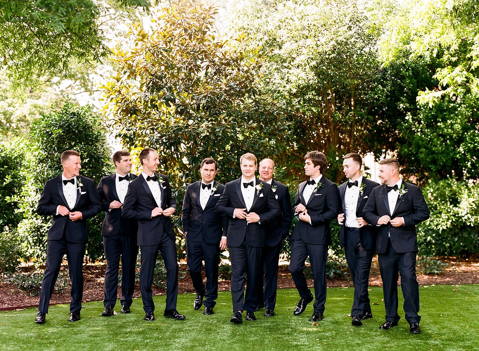 Merrimon Wynne groom walking and buttoning his jacket with his groomsmen photo