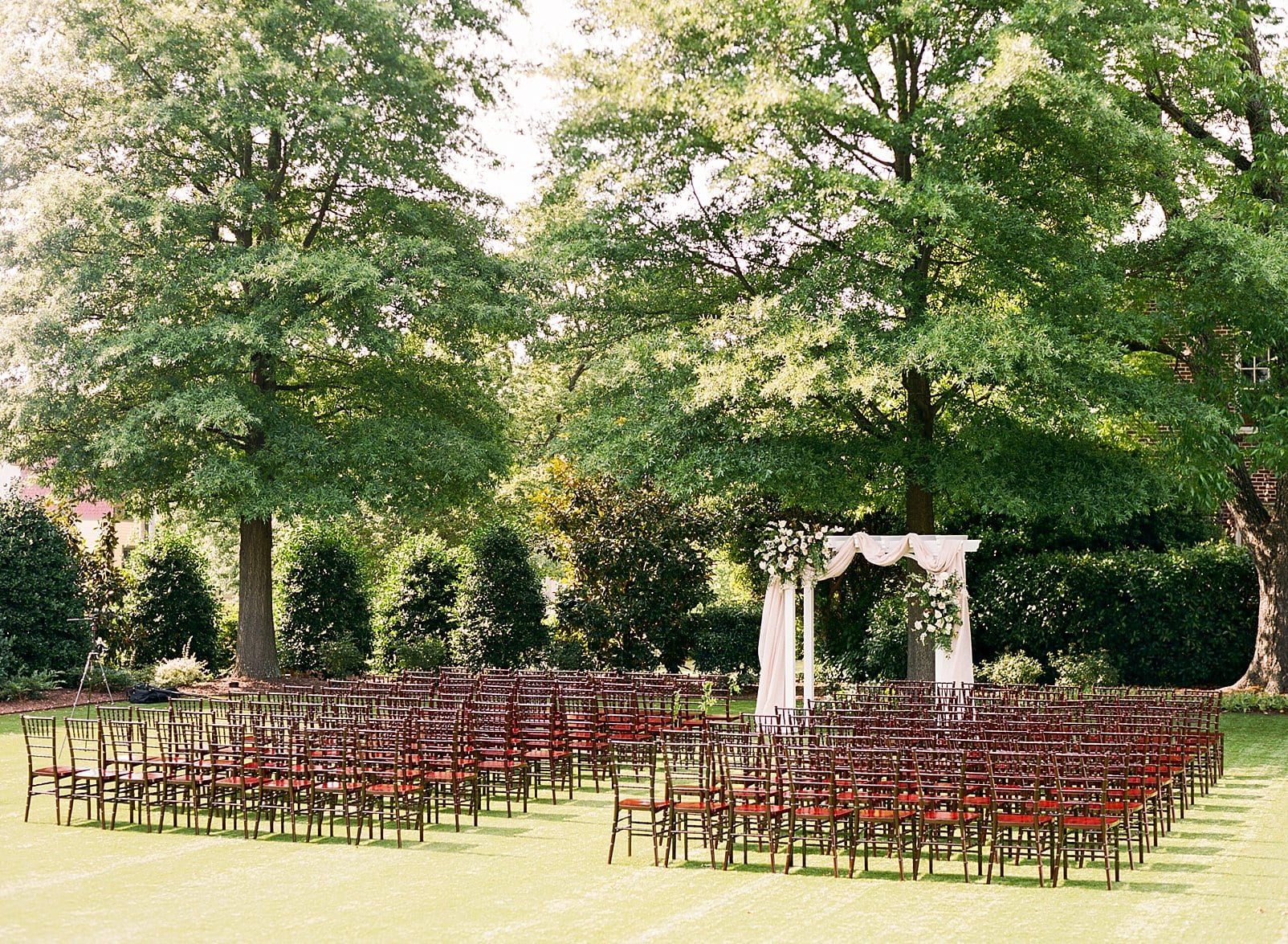 Merrimon Wynne wedding ceremony site with brown wooden chairs and a white arbor draped with cloth and decorated with flower installations photo