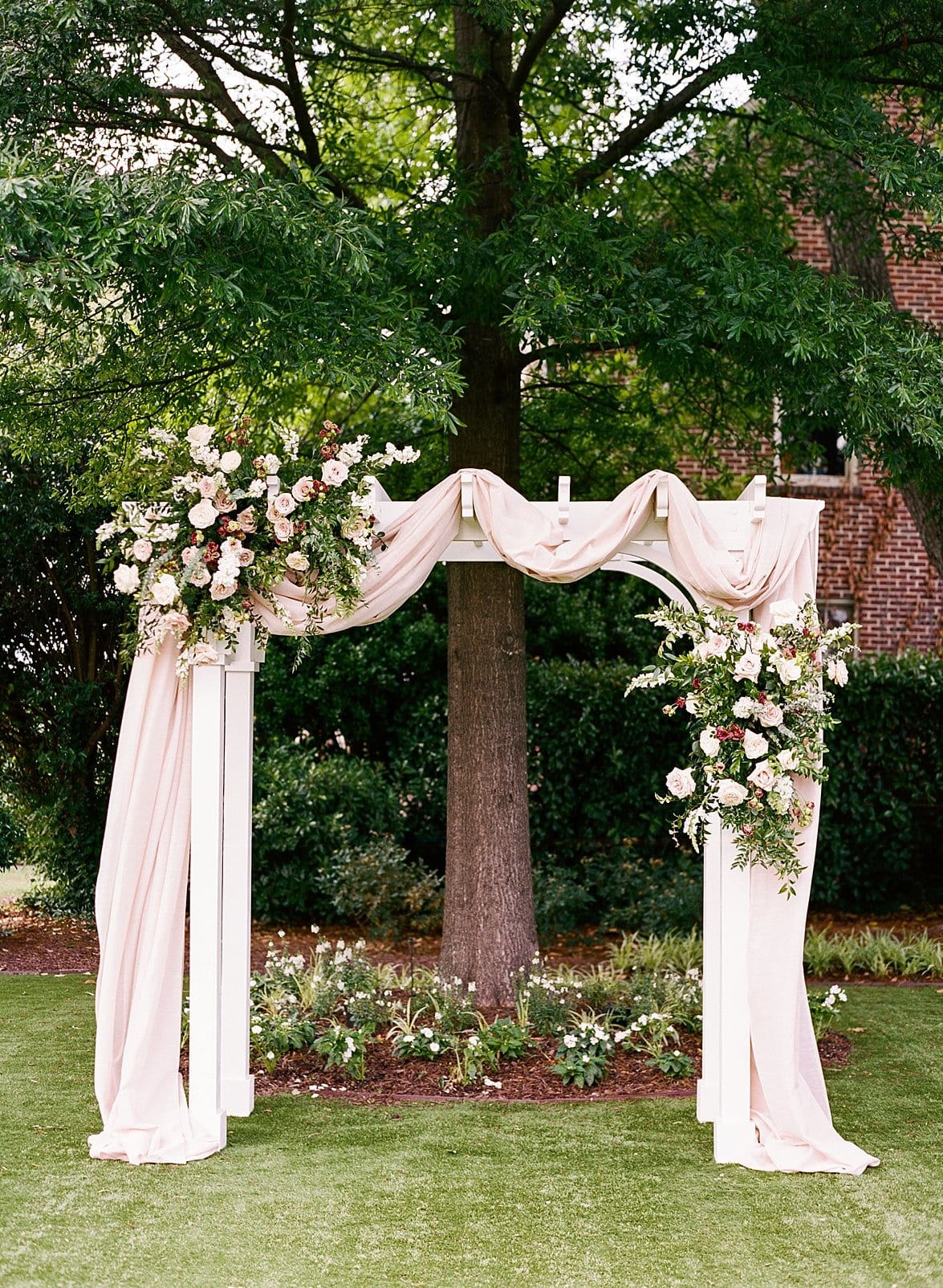 Merrimon Wynne white arbor with fabric draped across it behind the flower installations at the ceremony site photo