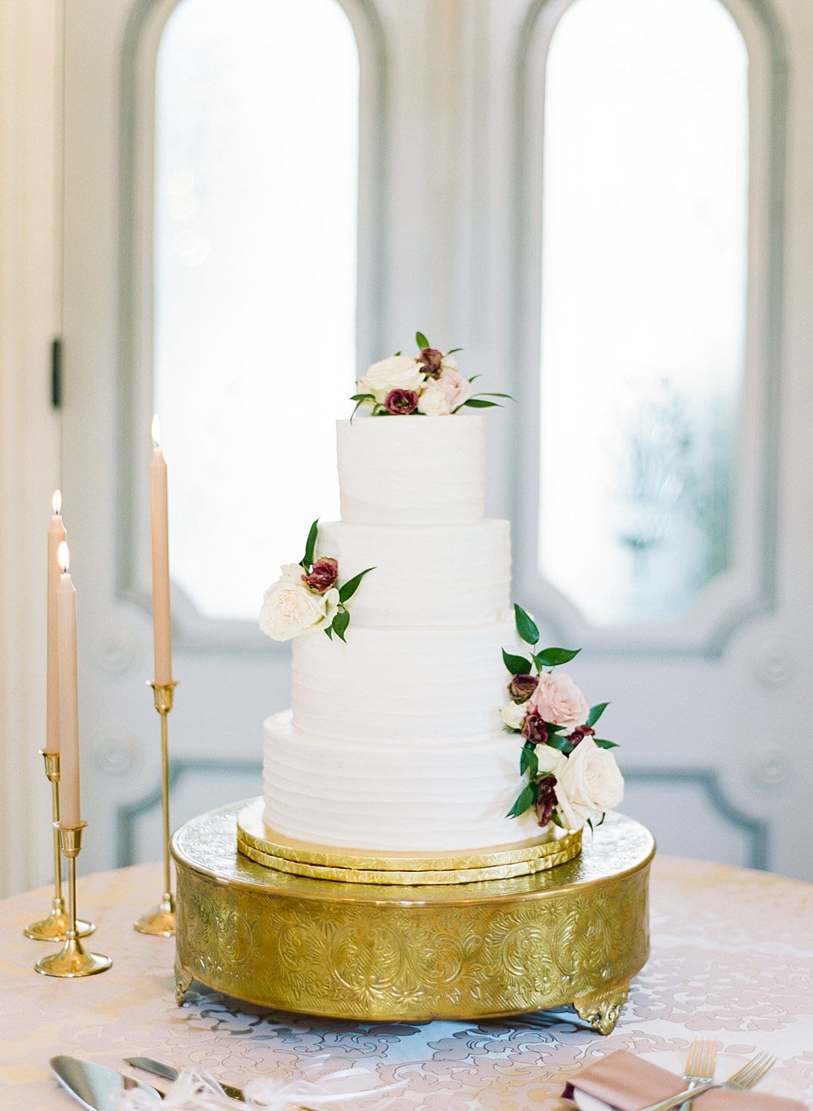 Edible Art white four tier wedding cake on a gold cake stand and decorated with fresh florals photo