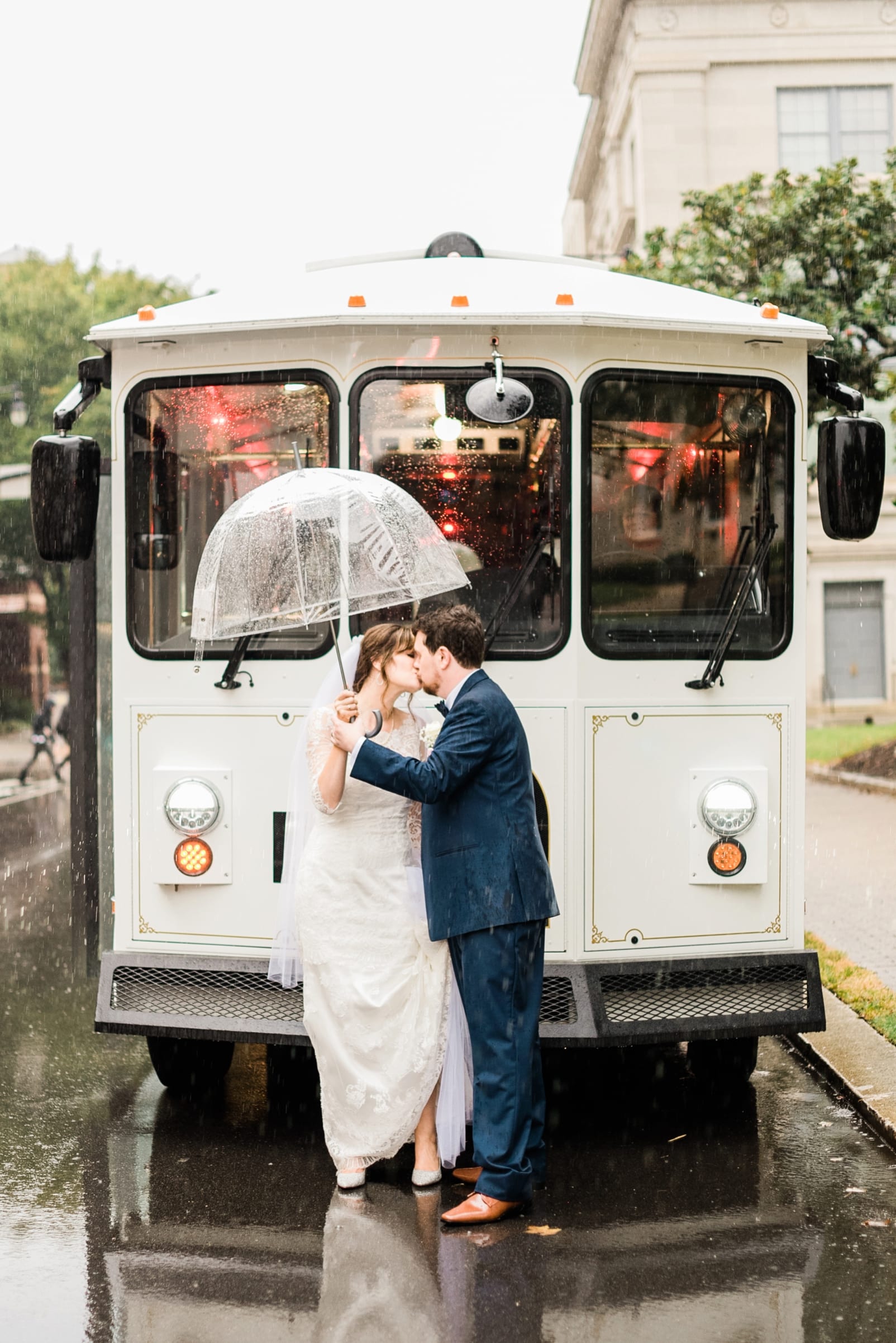 The great Raleigh trolley bride and groom kissing in front of his under a clear umbrella photo