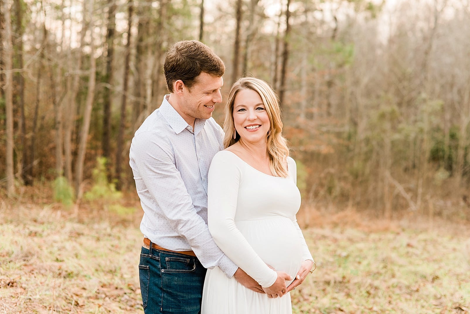Outdoor Raleigh mini session with the wife leaning against the husband while he looks down at the belly photo