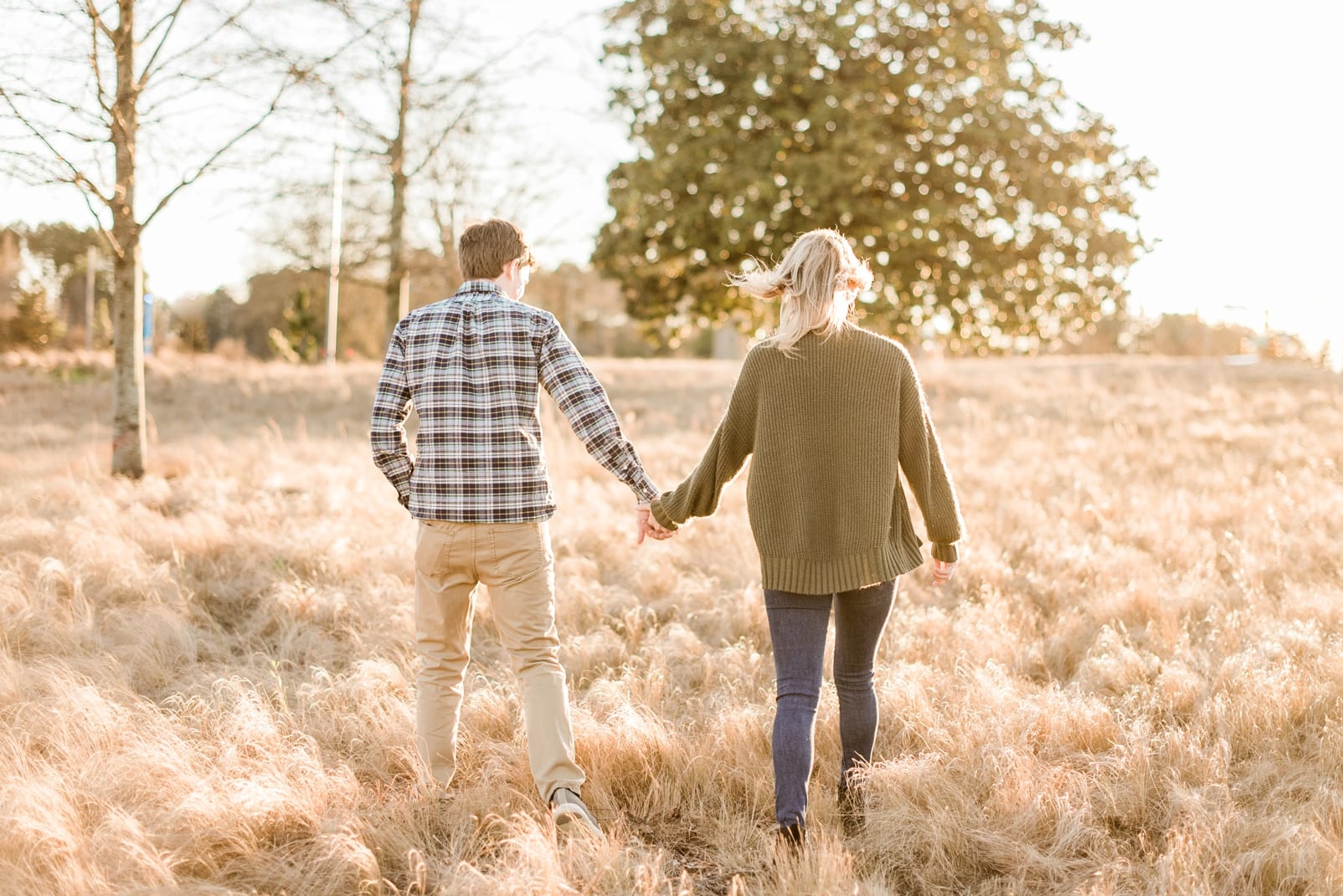 Winter engagement couple walking hand in hand through a grass field photo