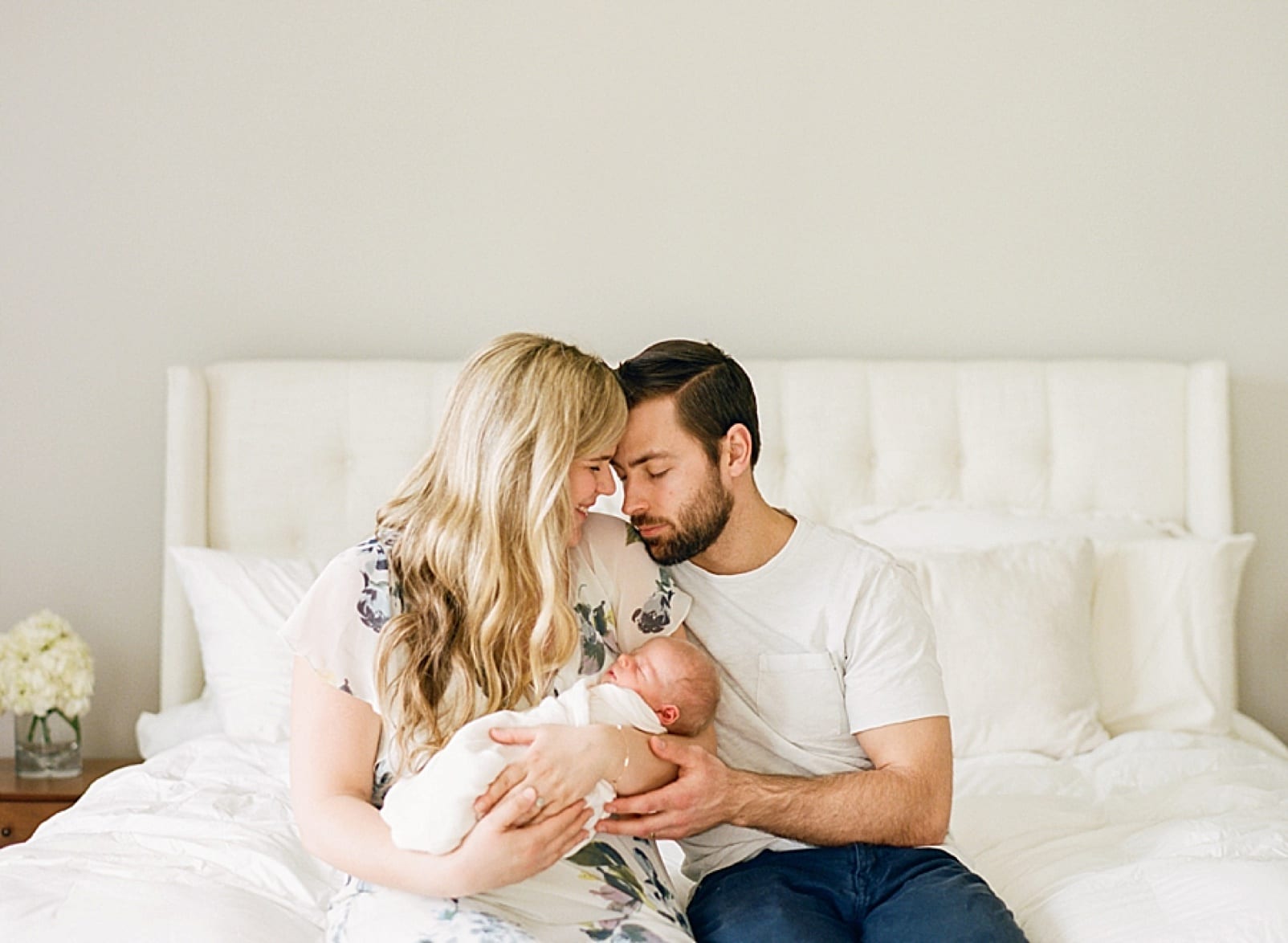 mother and father snuggling while holding their newborn son on the edge of their bed photo