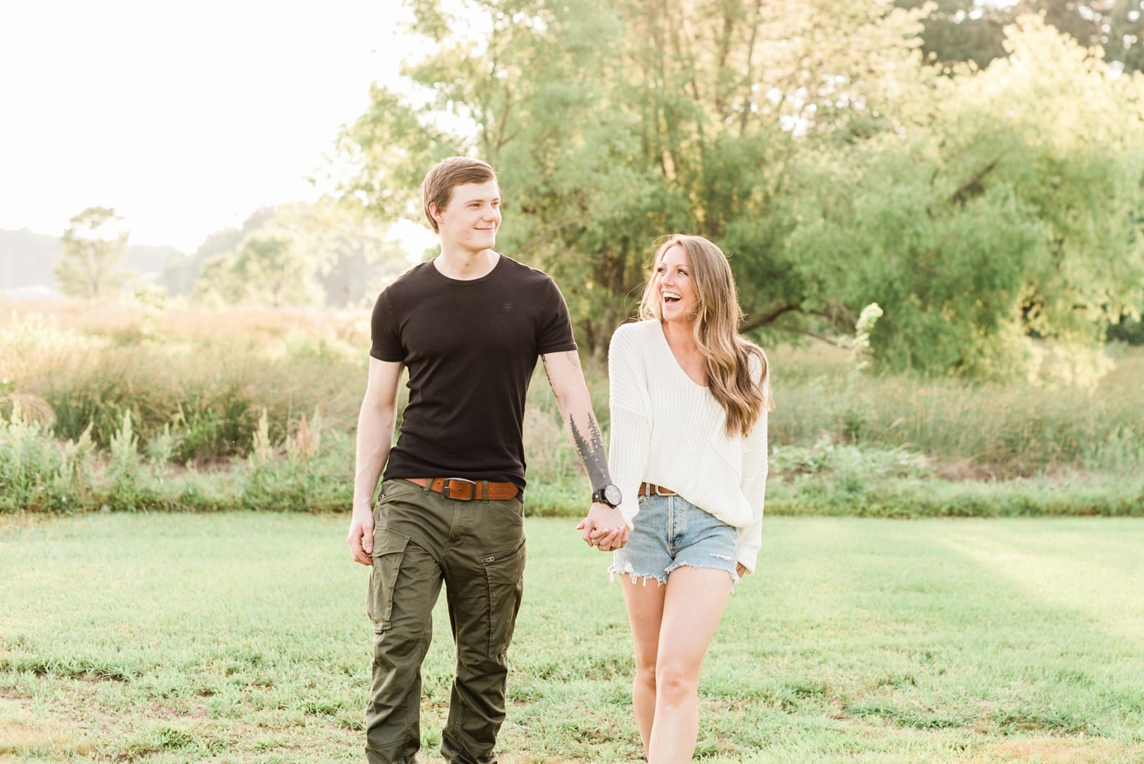 Raleigh future bride and groom holding hands while they laugh and walking next to a field photo