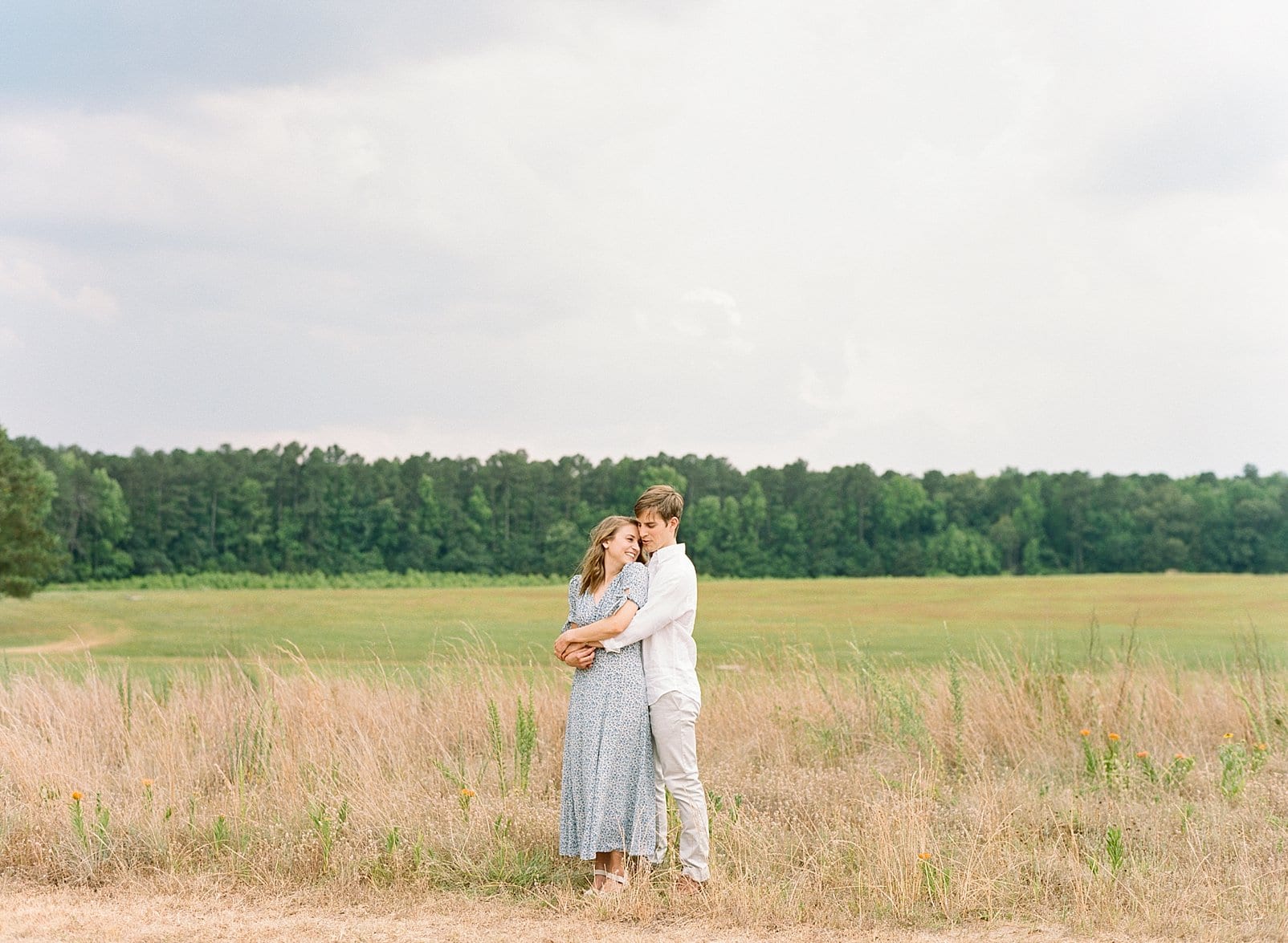 Raleigh film engagement session couple in the middle of a field with the trees in the background photo