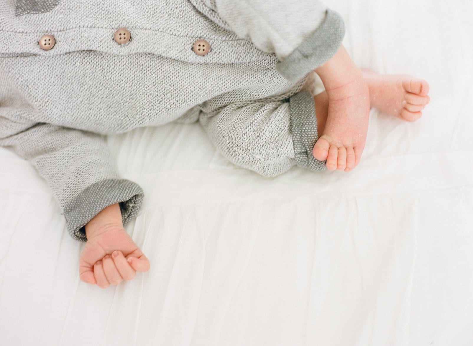 Raleigh newborn session baby boy in a grey button outfit and his feet curled up photo