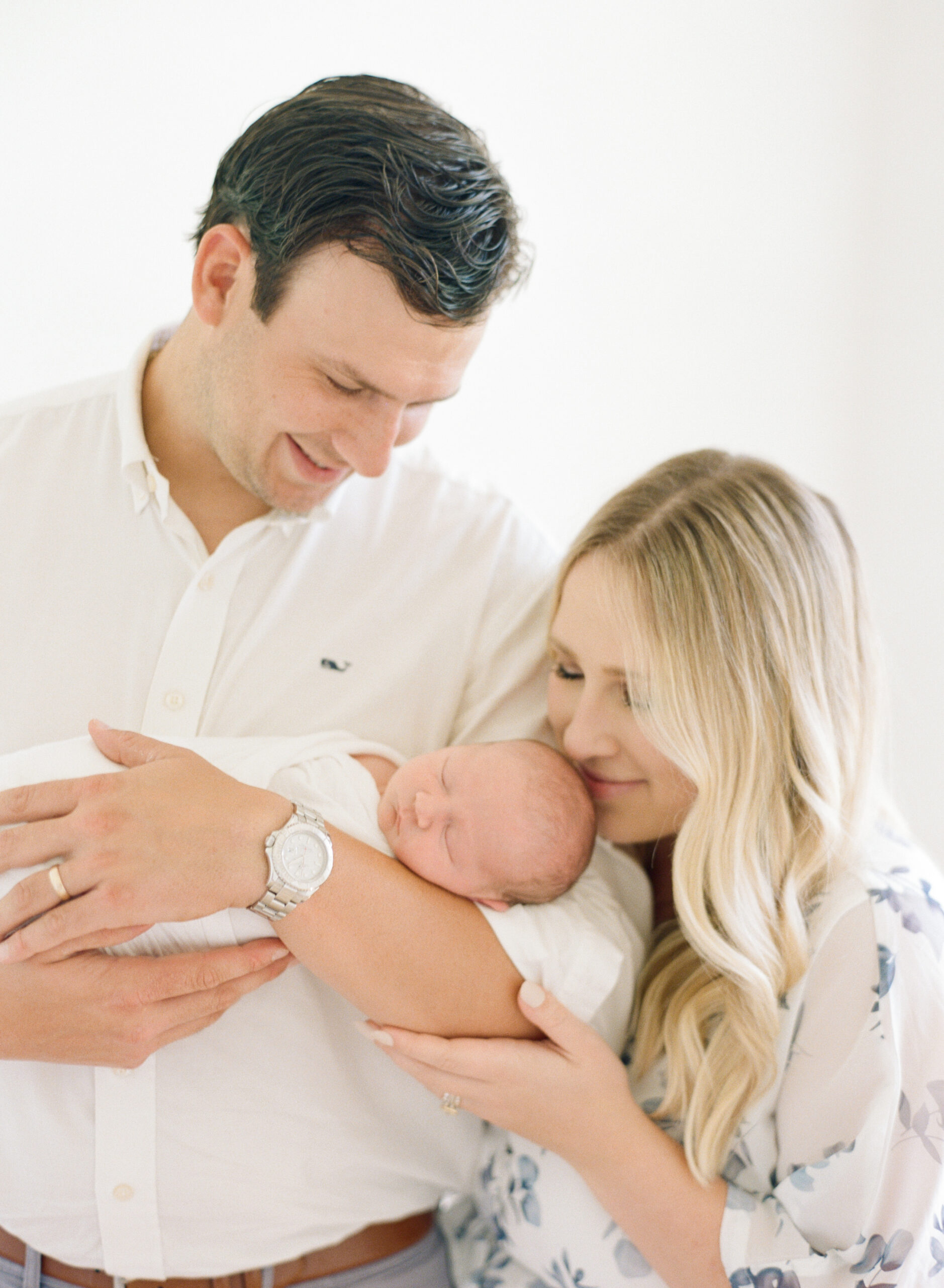 Mom and dad hold their newborn son and look lovingly over him during their Wake Forest newborn photography session. Photographed by Raleigh newborn photographer A.J. Dunlap Photography.