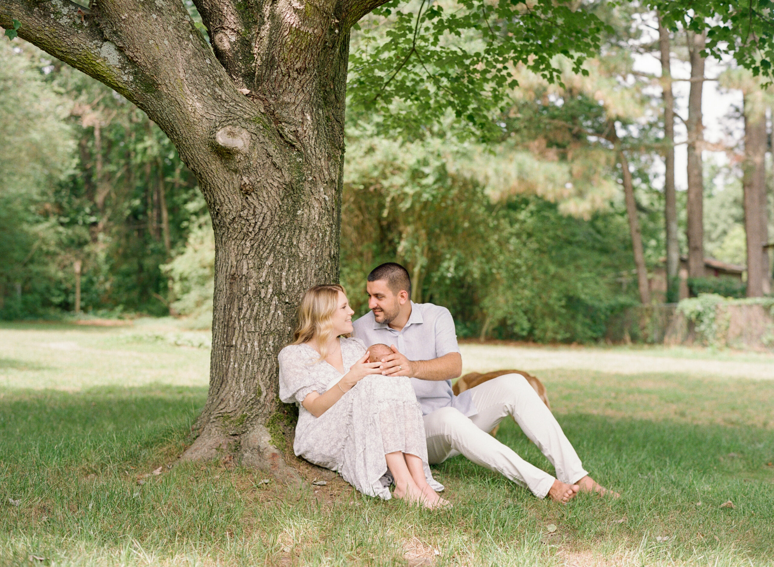 New parents sit under a tree holding their newborn son during his photo session. Image by newborn photographers in Raleigh A.J. Dunlap Photography.