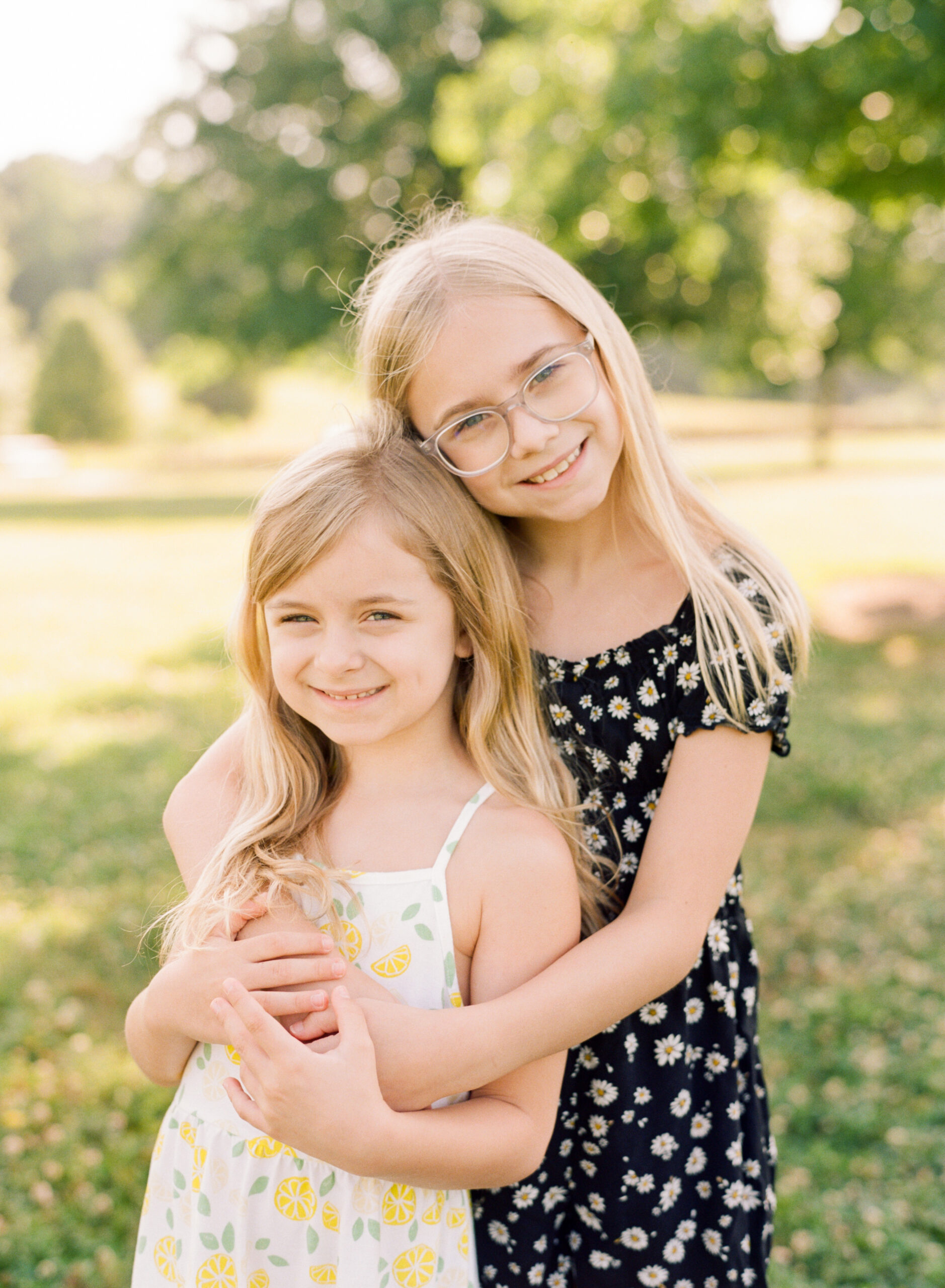 Sisters hug for a portrait at Joyner Park. Image by Wake Forest Family Photography photographer A.J. Dunlap.